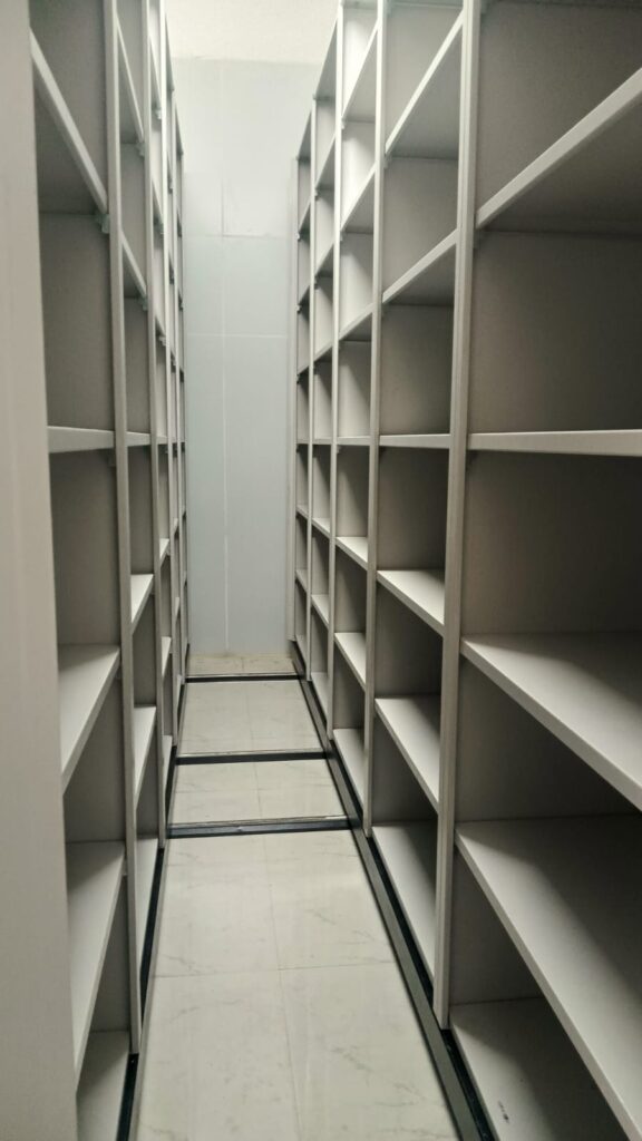 Interior view of 5 bay mechanical file compactor showing multi-level shelving on both sides with floor-mounted rail tracks installed at Gulbrandsen Technologies GIDC Jhagadia Bharuch Gujarat by Myriad Storage System